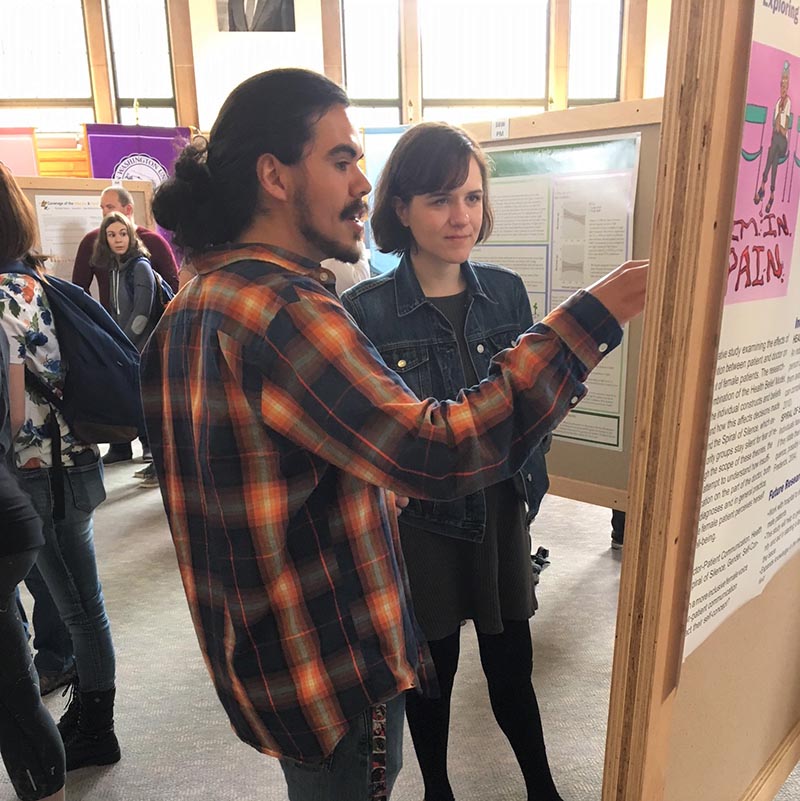 A student explains his research as another student looks intently at his poster