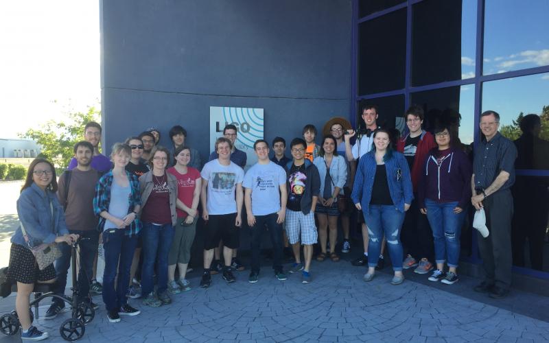 A large group of students and a professor posing in front of a building