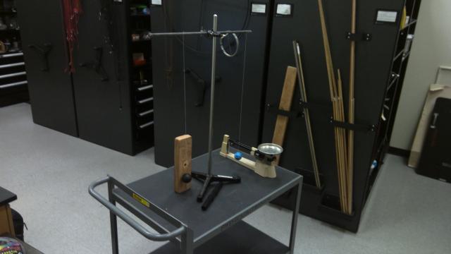 Two balls hang from a horizontal rod with a triple beam balance and block on the cart