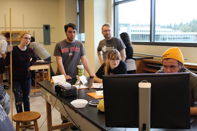Four students work in a physics lab while a TA looks on